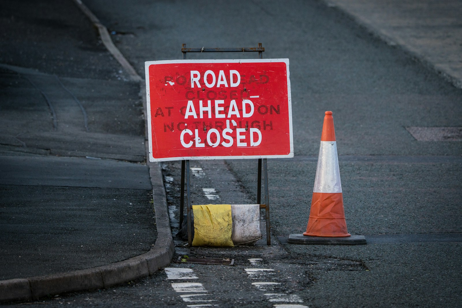 a road closed sign next to a traffic cone